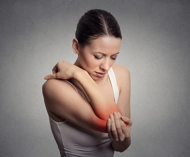Joint inflammation indicated with red spot on female's elbow. Arm pain and injury concept. Closeup portrait woman with painful elbow on gray background
